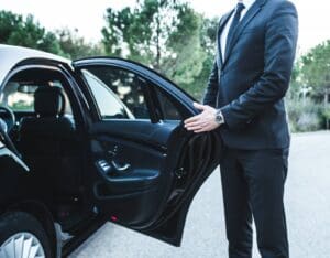 A man in a suit standing next to an open car door.