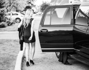 A woman in black dress walking towards a car.